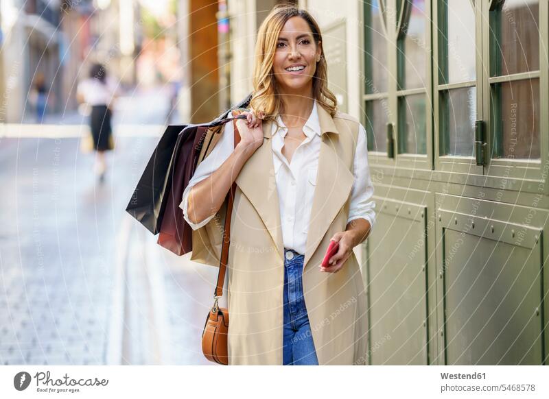 Frau trägt Einkaufstasche, während sie am Fussweg in der Stadt steht Farbaufnahme Farbe Farbfoto Farbphoto Außenaufnahme außen draußen im Freien Tag