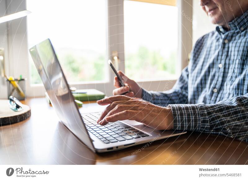 Älterer Mann benutzt Laptop und Smartphone zu Hause Leute Menschen People Person Personen Europäisch Kaukasier kaukasisch 1 Ein ein Mensch eine nur eine Person