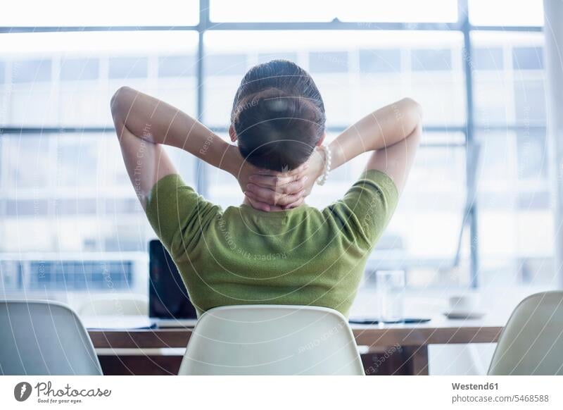 Müde Geschäftsfrau sitzt mit Händen hinter dem Nacken am Schreibtisch im Büro Farbaufnahme Farbe Farbfoto Farbphoto Innenaufnahme Innenaufnahmen innen drinnen