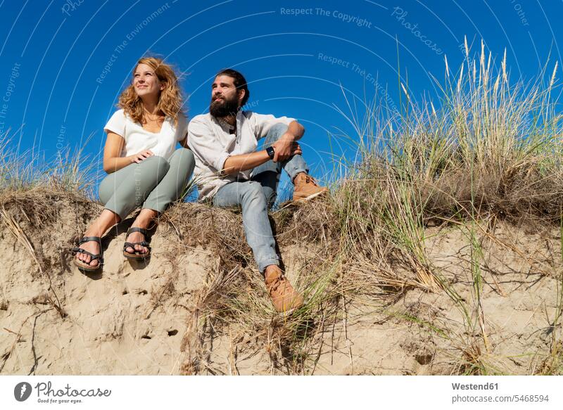 Junges Paar sitzt im Sommer auf einer Düne und entspannt sich sitzen sitzend erholen erholend Junge Paare Duenen Dünen Sommerzeit sommerlich Erholung