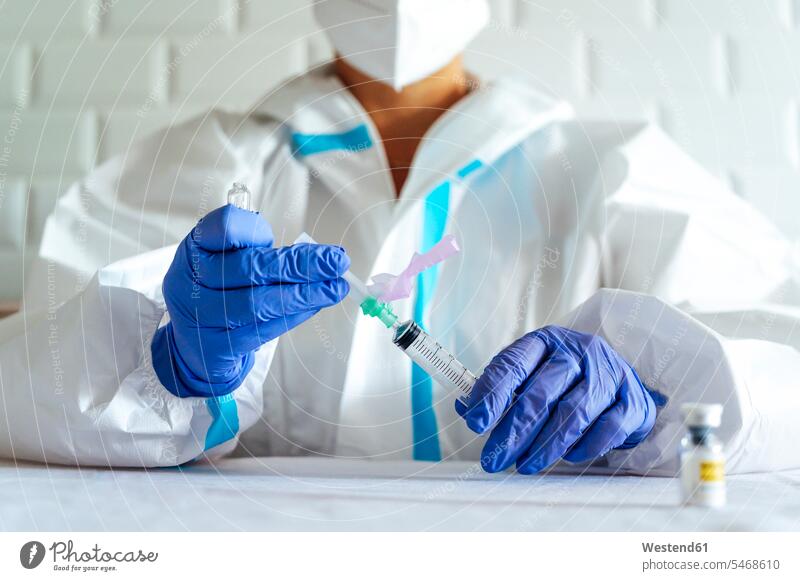 Krankenschwester in Arbeitsschutzkleidung füllt Injektion beim Sitzen am Tisch im Krankenhaus auf Farbaufnahme Farbe Farbfoto Farbphoto Innenaufnahme
