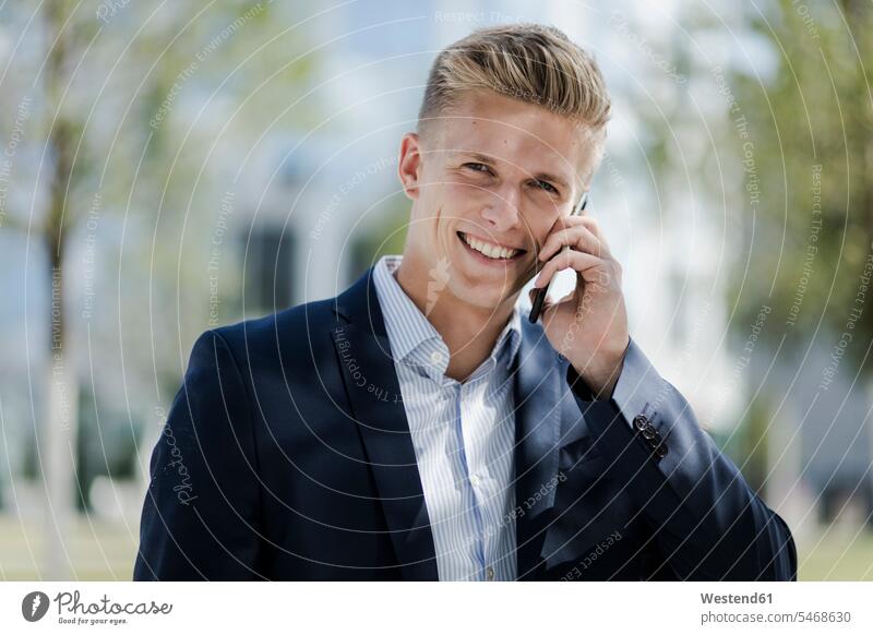 Porträt eines lächelnden jungen Geschäftsmannes beim Telefonieren Job Berufe Berufstätigkeit Beschäftigung Jobs geschäftlich Geschäftsleben Geschäftswelt