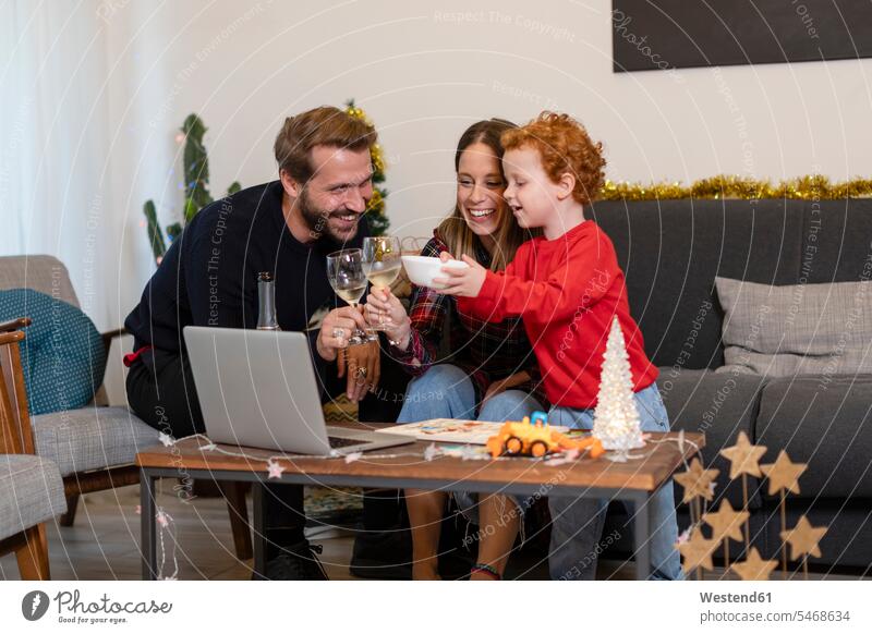 Fröhliche Familie stößt während der Weihnachtsfeier zu Hause mit Videogesprächen über Laptop auf Getränke an Farbaufnahme Farbe Farbfoto Farbphoto