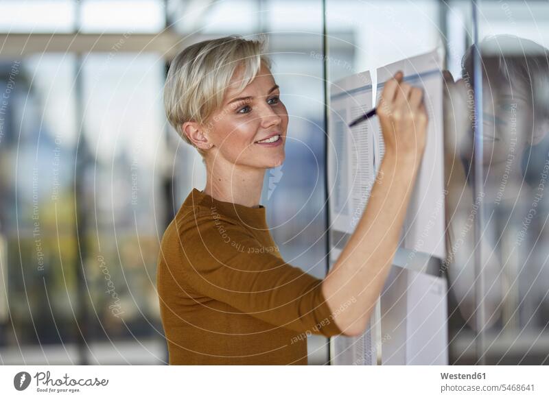 Lächelnde Geschäftsfrau schreibt auf Papiere an Glasscheibe Glasscheiben Zuversicht Zuversichtlich Selbstvertrauen selbstbewusst Vertrauen Geschäftsfrauen
