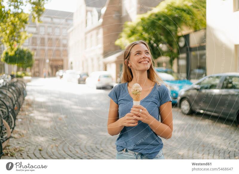 Niederlande, Maastricht, lächelnde blonde junge Frau hält Eiswaffel in der Stadt Eistüte Eistuete halten blonde Haare blondes Haar staedtisch städtisch weiblich