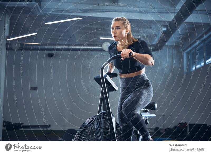 Athletische Frau beim Airbike-Training im Fitnessstudio weiblich Frauen Ausdauer Ausdauernd Fitnessclubs Fitnessstudios Turnhalle Bewegung sich bewegen Fahrrad