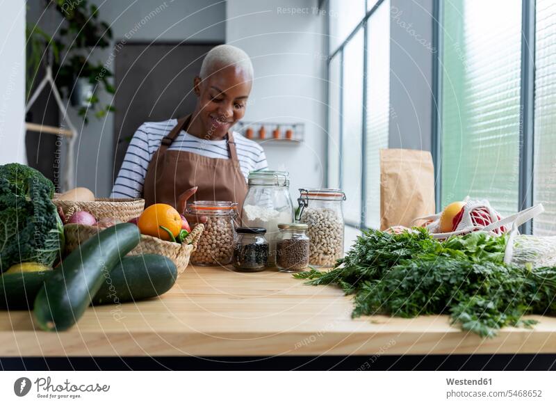 Frau mit Schürze in der Küche , Auspacken frisch gekauften Bio-Obst und Gemüse Leute Menschen People Person Personen Afrikanisch Afrikanische Abstammung