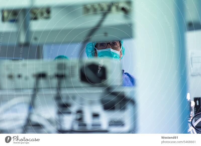 Fokussierter männlicher Chirurg mit Blick auf Überwachungsgeräte während der Operation auf der Intensivstation Farbaufnahme Farbe Farbfoto Farbphoto