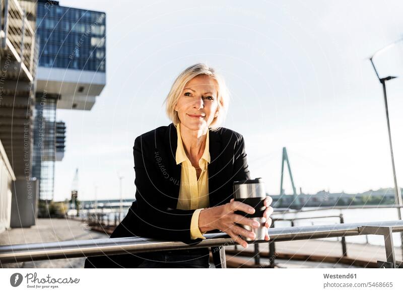 Lächelnde ältere Geschäftsfrau mit Kaffee zum Mitnehmen am Flussufer Geschäftsfrauen Businesswomen Businessfrauen Businesswoman Zuversicht Zuversichtlich