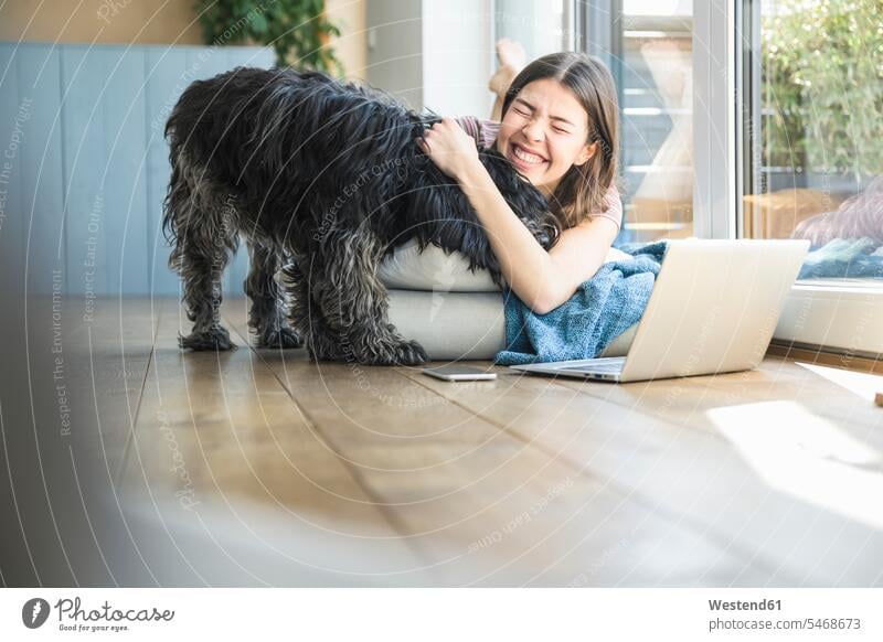 Glückliche junge Frau mit Hund am Fenster liegend zu Hause glücklich glücklich sein glücklichsein weiblich Frauen Zuhause daheim liegt Hunde Erwachsener