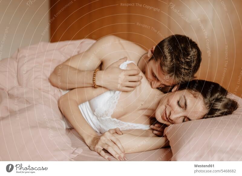 Intimes junges Paar im Bett liegend Betten anfassen Berührung knuddeln schmusen Kuss Küsse geniessen Genuss Glück glücklich sein glücklichsein intim Intimitaet