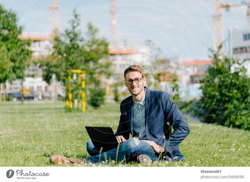 Junger Geschäftsmann sitzt im Park, mit Laptop Gras Parkanlagen Parks Schneidersitz junger Mann junge Männer Notebook Laptops Notebooks Businessmann