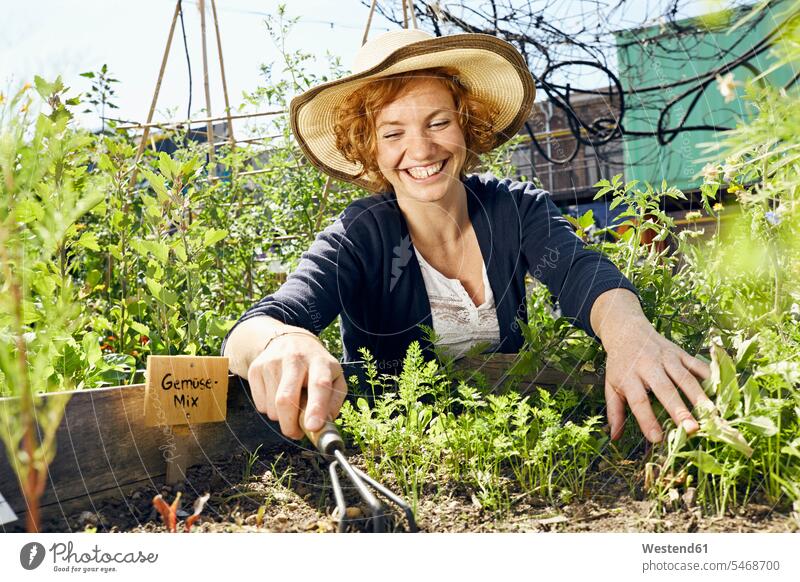 Glückliche junge Frau mit Strohhut im Stadtgarten Urban Gardening Urbaner Gartenbau weiblich Frauen Strohhüte Strohhuete glücklich glücklich sein glücklichsein