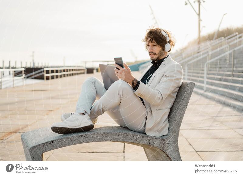 Porträt eines schockierten Geschäftsmannes mit Kopfhörer und Laptop, der auf sein Mobiltelefon schaut geschäftlich Geschäftsleben Geschäftswelt Geschäftsperson