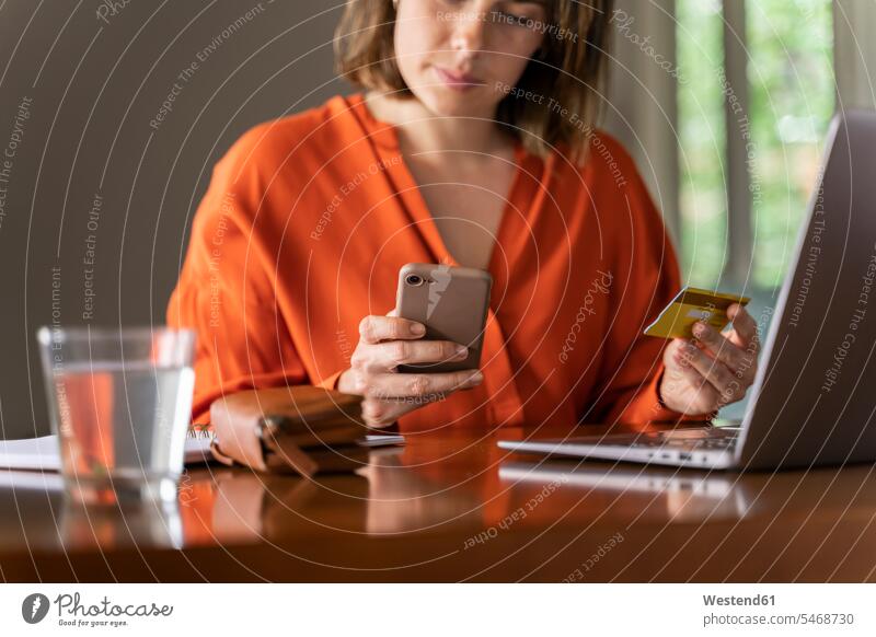 Geschäftsfrau mit Kreditkarte, die zu Hause ein Smartphone benutzt Farbaufnahme Farbe Farbfoto Farbphoto Innenaufnahme Innenaufnahmen innen drinnen Tag