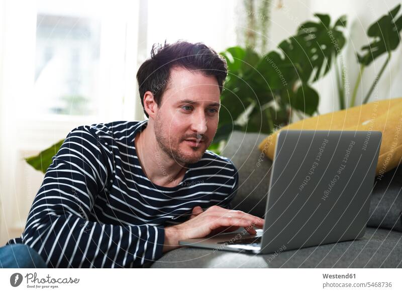 Mann sitzt zu Hause und benutzt Laptop sitzen sitzend Laptop benutzen Laptop benützen Männer männlich Notebook Laptops Notebooks Erwachsener erwachsen Mensch