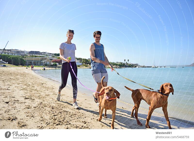 Junges Paar geht mit Hund am Strand spazieren Hunde gehen gehend Pärchen Paare Partnerschaft Beach Straende Strände Beaches Haustier Haustiere Tier Tierwelt