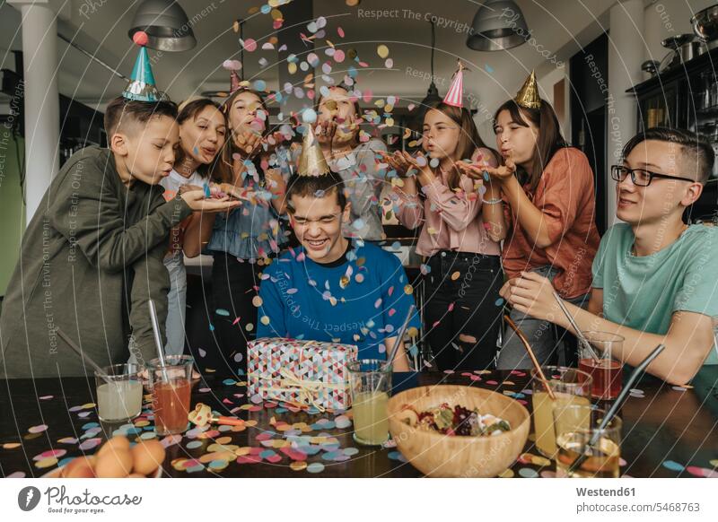 Freunde werfen Konfetti auf Geburtstagskind, das mit einem Geschenk am Esstisch sitzt Farbaufnahme Farbe Farbfoto Farbphoto Deutschland Innenaufnahme
