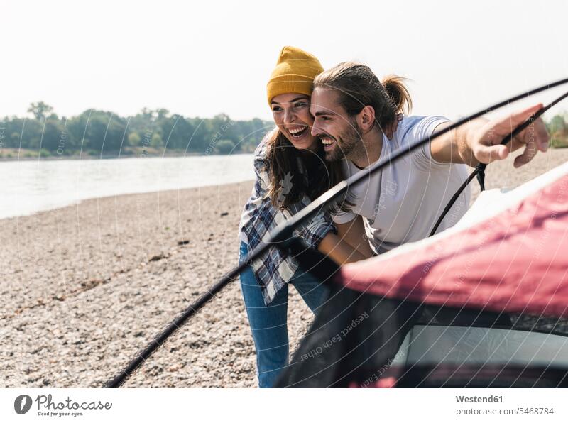 Glückliches junges Paar baut ein Zelt am Flussufer auf glücklich glücklich sein glücklichsein Pärchen Paare Partnerschaft aufbauen Zelte Ufer Mensch Menschen