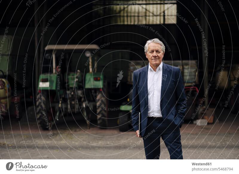 Porträt eines leitenden Geschäftsmannes mit Laptop auf einem Bauernhof mit Traktor in der Scheune Job Berufe Berufstätigkeit Beschäftigung Jobs geschäftlich