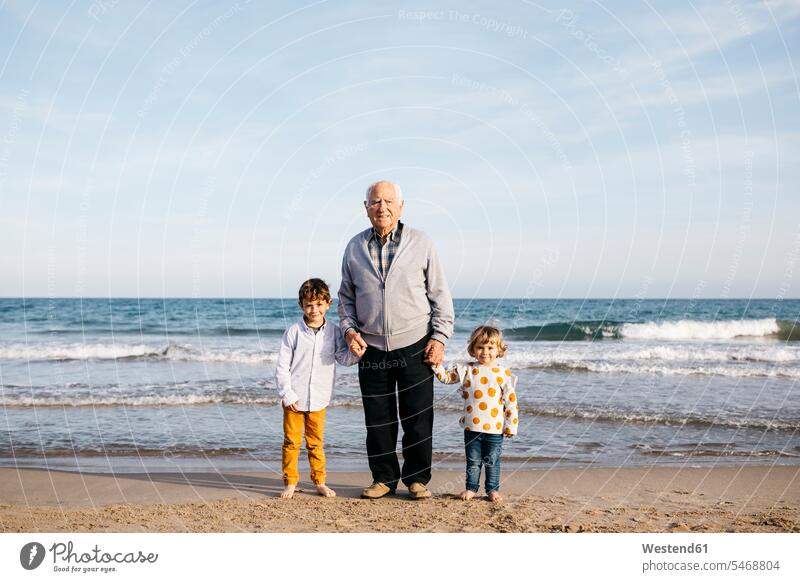 Porträt eines glücklichen Großvaters, der Hand in Hand mit seinen Enkeln am Strand steht Spanien Senior ältere Männer älterer Mann Senioren Junge Buben Knabe