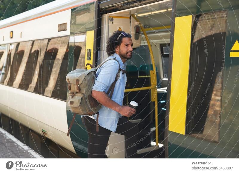 Junger trendiger Mann steigt am Bahnhof in den Zug Farbaufnahme Farbe Farbfoto Farbphoto Außenaufnahme außen draußen im Freien Tag Tageslichtaufnahme