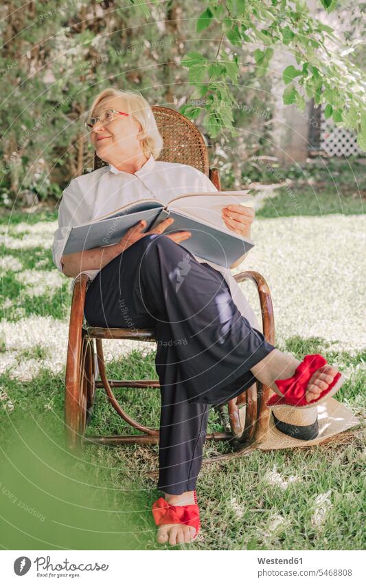 Ältere Frau hält Buch und schaut weg, während sie sich auf einem Stuhl im Hof entspannt Farbaufnahme Farbe Farbfoto Farbphoto Spanien Freizeitbeschäftigung Muße
