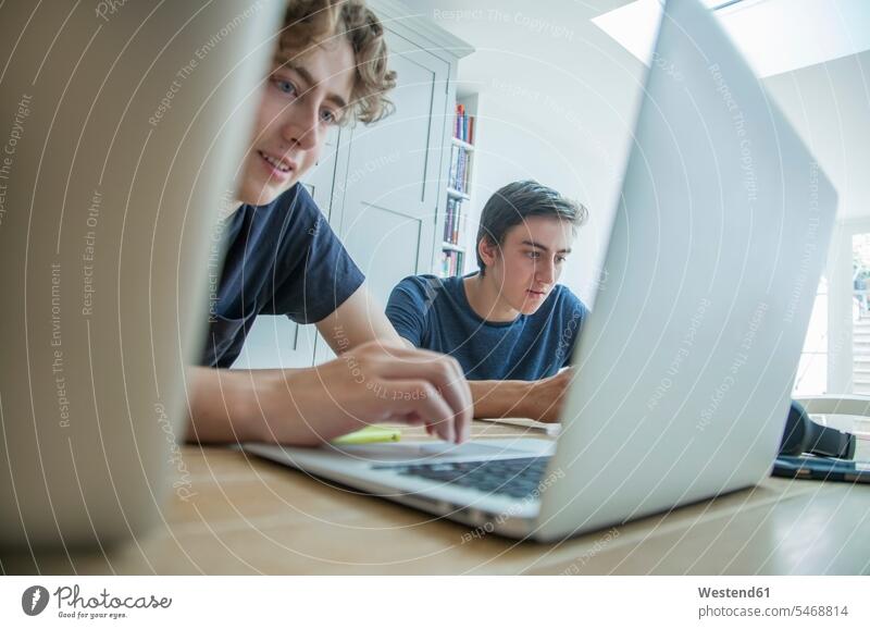 Zwei Jungen im Teenager-Alter benutzen zu Hause Laptop und Tablett auf dem Tisch Freunde Schüler Student T-Shirt Kopfhörer Handy arbeiten lernen lächeln sitzen