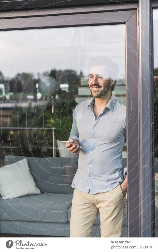 Junger Mann schaut aus dem Fenster, benutzt Smartphone Deutschland Drahtlose Technologie drahtlose Verbindung Drahtlose Kommunikation schnurlose Verbindung