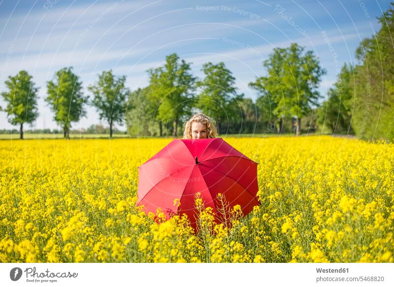 Reife Frau mit rotem Regenschirm steht inmitten von Ölsaaten-Raps gegen den Himmel Farbaufnahme Farbe Farbfoto Farbphoto Deutschland Freizeitbeschäftigung Muße