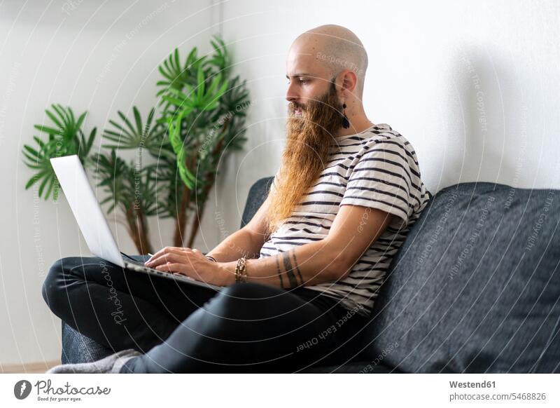Hipster sitzt auf Couch zu Hause mit Laptop mobiles Arbeiten mobile working Individualität Individuell Blick nach unten Freizeitkleidung casual