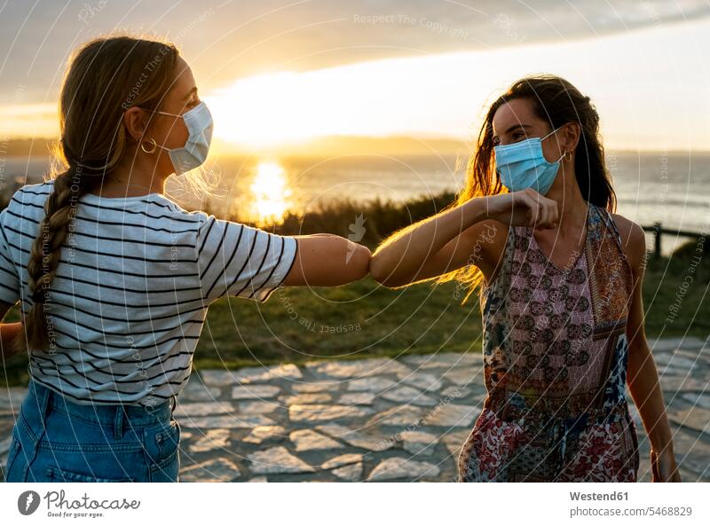 Frauen mit schützenden Gesichtsmasken, die während des COVID-19-Ausbruchs mit dem Ellbogen gegen den Himmel stoßen Farbaufnahme Farbe Farbfoto Farbphoto