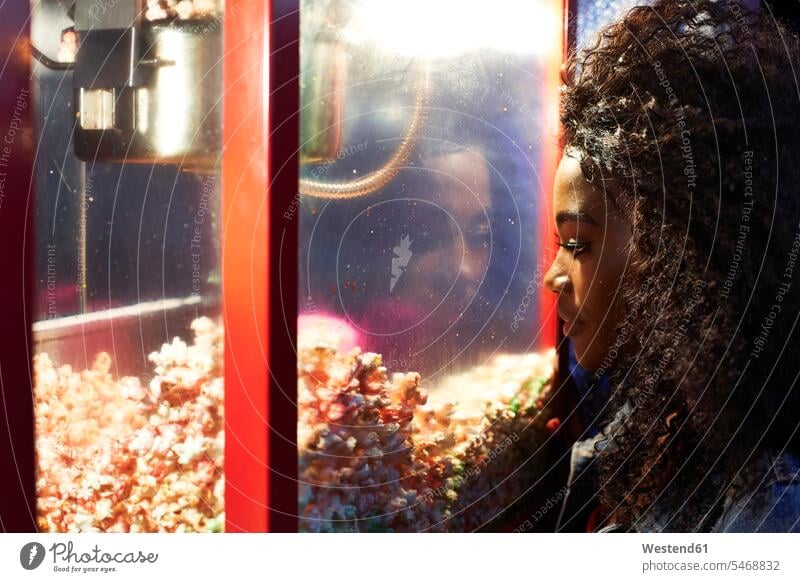 Junge Frau betrachtet Popcorn in Glasvitrine auf der Messe Leute Menschen People Person Personen Afrikanisch Afrikanische Abstammung dunkelhäutig Farbige