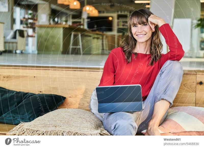 Frau benutzt digitales Tablet, während sie im modernen Büro sitzt Farbaufnahme Farbe Farbfoto Farbphoto Innenaufnahme Innenaufnahmen innen drinnen Tag