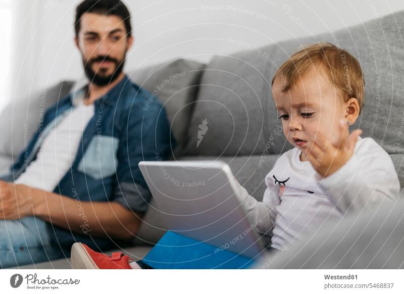Vater sitzt auf dem Sofa, während die Tochter auf die Tafel schaut betrachten betrachtend Papas Väter Vati Vatis Papis Tablet Tablet Computer Tablet-PC