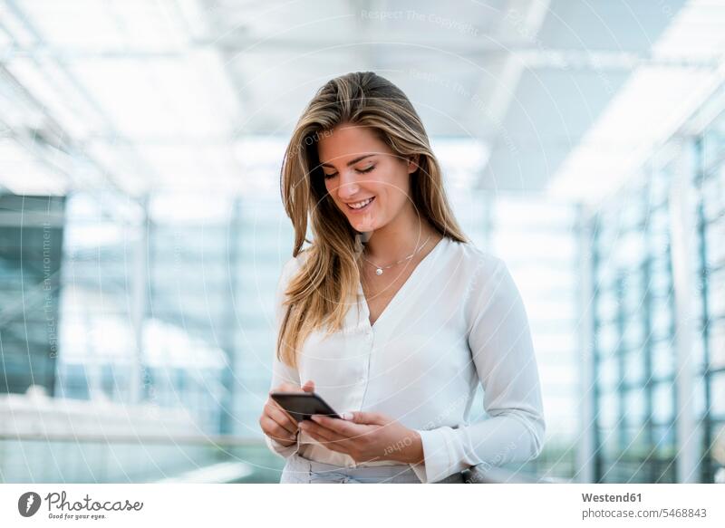 Lächelnde junge Frau steht am Geländer und benutzt ihr Handy Mobiltelefon Handies Handys Mobiltelefone Geschäftsfrau Geschäftsfrauen Businesswomen