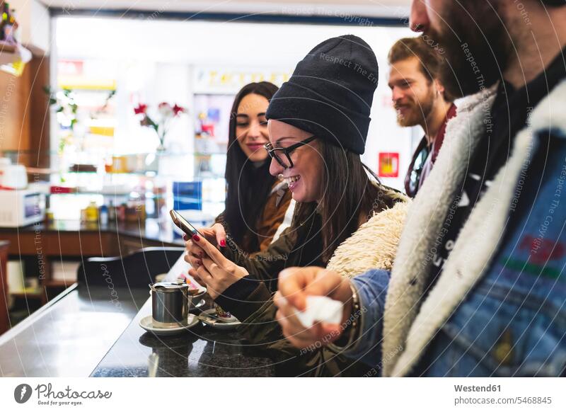 Lächelnde Frau benutzt Smartphone, während sie sich mit Freunden im Café vergnügt Farbaufnahme Farbe Farbfoto Farbphoto Freizeitbeschäftigung Muße Zeit