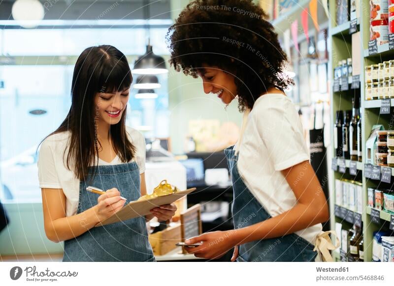 Zwei lächelnde Frauen in einem Geschäft mit Zwischenablage Shop Laden Läden Geschäfte Shops Klemmbrett Klemmbretter weiblich Einzelhandel Handel handeln