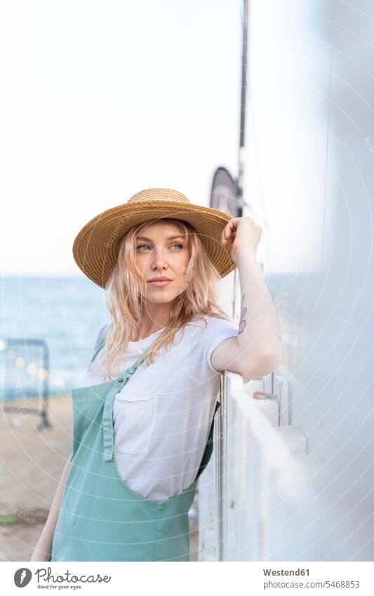 Junge Frau verbringt einen Tag am Meer, mit Strohhut entspannen relaxen stehend steht Muße Stil stylisch Lifestyles Beach Beaches Straende Strände außen draußen