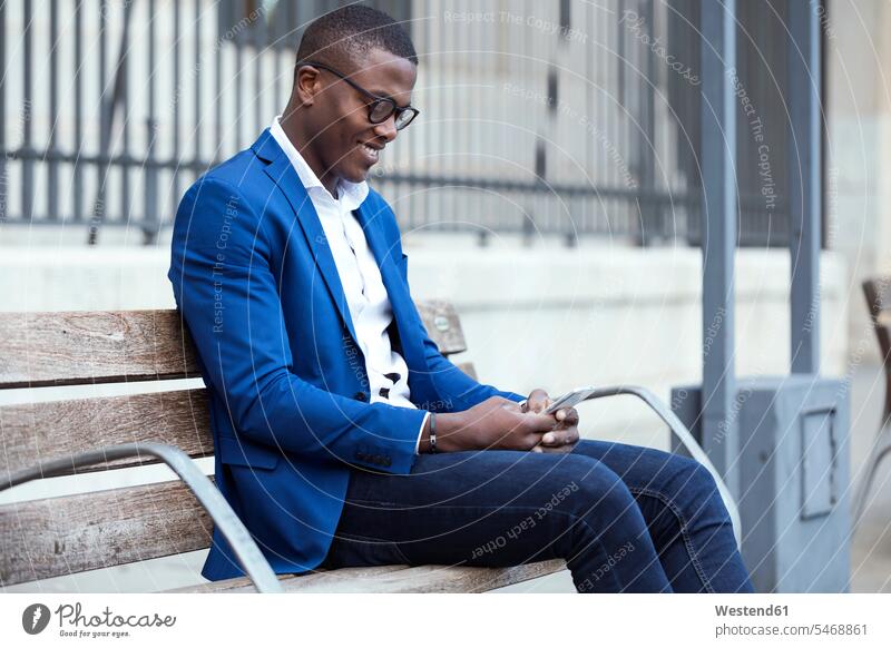 Junger Geschäftsmann in blauer Anzugjacke sitzt auf Bank und benutzt Smartphone Job Berufe Berufstätigkeit Beschäftigung Jobs geschäftlich Geschäftsleben