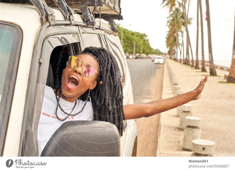 Porträt einer schreienden Frau mit Dreadlocks, die sich aus dem Autofenster lehnt, Maputo, Mosambik T-Shirts KFZ Verkehrsmittel Automobil Autos PKW PKWs Wagen