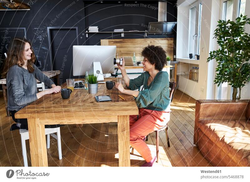 Zwei glückliche junge Frauen mit Kamera im modernen Büro Fotoapparat Fotokamera Office Büros weiblich Glück glücklich sein glücklichsein Arbeitsplatz