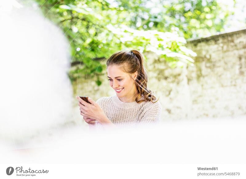 Lächelnde Frau betrachtet Mobiltelefon im Freien Smartphone iPhone Smartphones ansehen weiblich Frauen lächeln Handy Handies Handys Mobiltelefone Telefon
