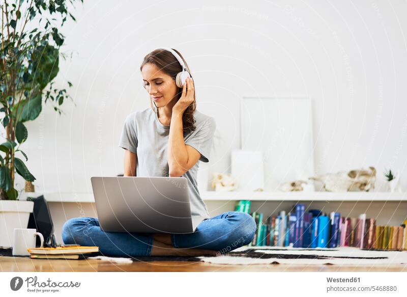 Entspannte junge Frau zu Hause, die mit Laptop auf dem Boden sitzt und Musik hört entspannt Zuhause sitzen hören Entspannung Computer Erwachsener Mensch