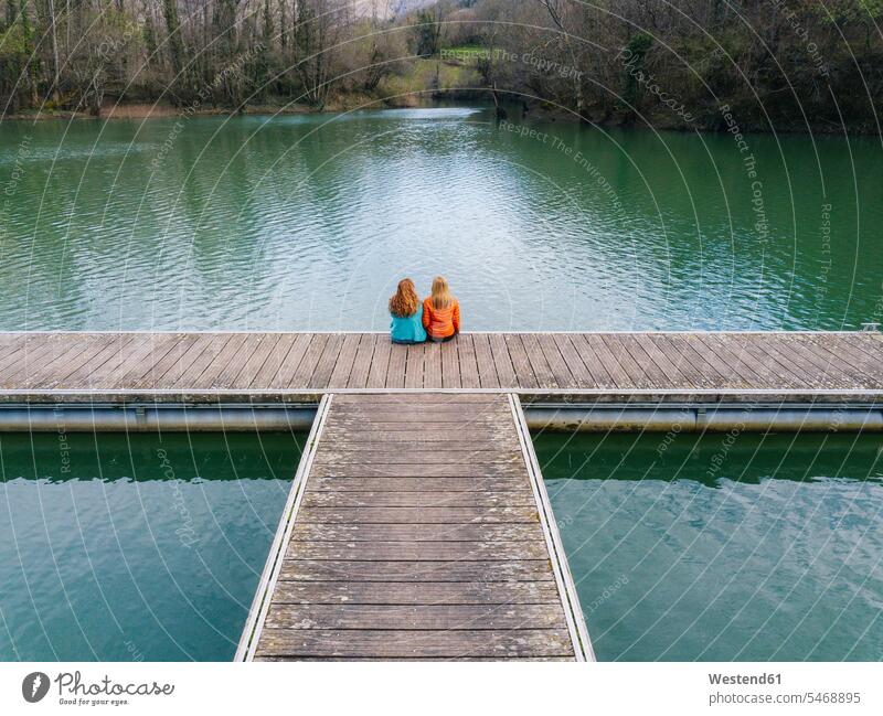 Rückenansicht von zwei Freunden, die nebeneinander auf dem Steg sitzen, Valdemurio-Stausee, Asturien, Spanien entspannen relaxen sitzend sitzt geniessen Genuss