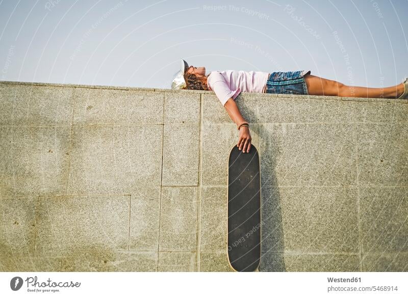 Mädchen mit Skateboard an der Wand liegend liegt Pause Pause machen Basecap Schirmmuetze Mütze Schirmmütze Muetze Kopfbedeckung Freizeit Muße Skateboarderin