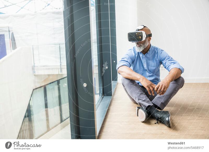 Geschäftsmann mit VR-Brille sitzt auf dem Boden am Fenster Virtuelle Realität Virtuelle Realitaet Böden Boeden sitzen sitzend Businessmann Businessmänner