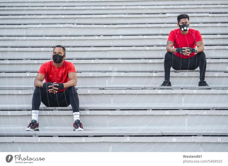 Zwei maskierte Sportler sitzen auf einer Treppe Freunde Kameradschaft Handschuhe sitzend sitzt Farben Farbtoene Farbton Farbtöne rote roter rotes Muße