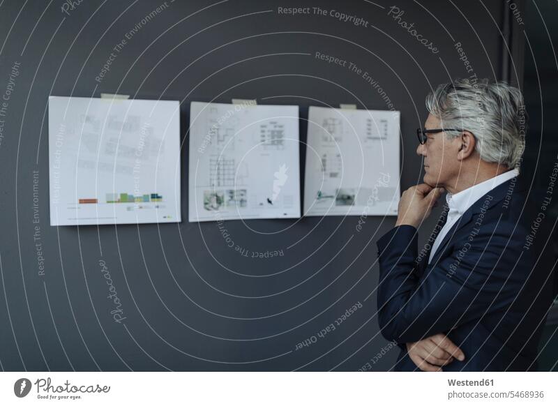 Leitender Geschäftsmann schaut auf Papiere, die an der Wand hängen Job Berufe Berufstätigkeit Beschäftigung Jobs Architekten geschäftlich Geschäftsleben