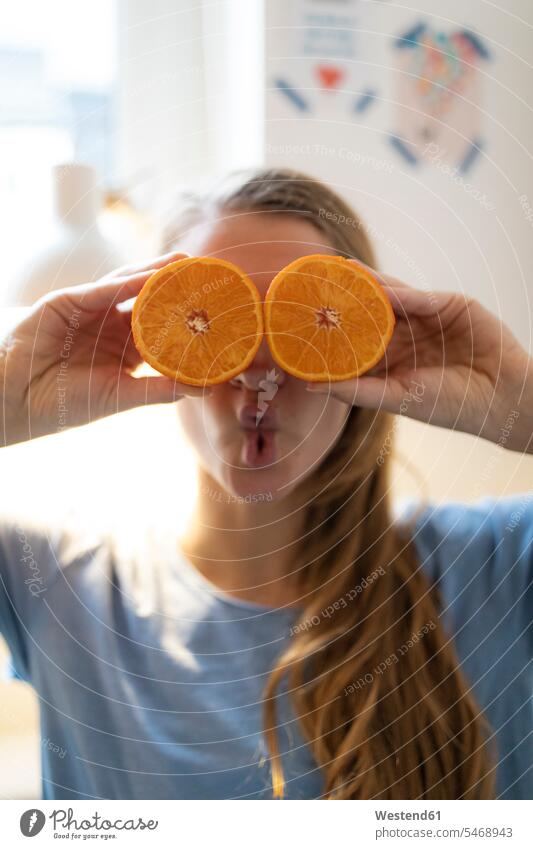 Verspielte junge Frau, die zu Hause ihre Augen mit Orangen bedeckt Leute Menschen People Person Personen Alleinstehende Alleinstehender Singles Unverheiratete